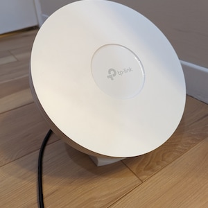 Może przedstawiać: Biały, okrągły router Wi-Fi TP-Link z czarnym kablem zasilającym.