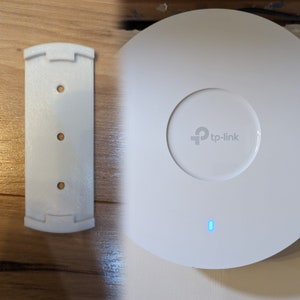 Puede incluir: Router inalámbrico blanco de montaje en el techo con un logotipo de tp-link y un indicador luminoso azul. El router viene con un soporte de pared de plástico blanco.
