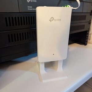 May include: A white TP-Link Omada Hard Router OC300 with a white stand. The router is mounted on a black network switch.