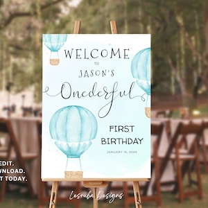 May include: A blue and white welcome sign with a watercolour design of hot air balloons. The sign says "Welcome to Jason's One-derful First Birthday January 16, 20XX".