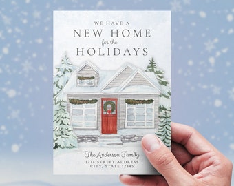 May include: A watercolor illustration of a snowy house with a red door and a wreath. The text reads "We have a new home for the holidays." The Anderson Family, 1234 Street Address, City, State 12345. Lesruba Designs.