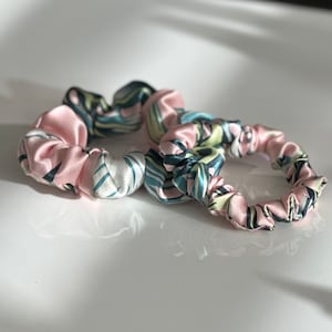 May include: Two hair scrunchies, one pink and one with a green, blue and white abstract pattern.