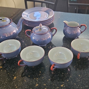 Może przedstawiać: Zestaw do herbaty w kolorze niebieskim i białym, składający się z czajnika, cukiernicy, dzbanka na śmietanę i czterech filiżanek. Zestaw ma kwiatowy wzór i błyszczące wykończenie.