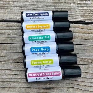 May include: Six essential oil roller bottles with labels for Love Your Lymph, Immune Support, Headache Aid, Deep Sleep, Tummy Tamer, and Menstrual Cramp Relief. Each bottle has a black cap and a white label with the name of the blend and the words "Roll-On Blend".