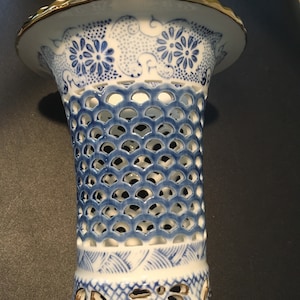 May include: A white ceramic vase with a blue and white floral pattern and a gold rim. The vase has a lattice design and is perfect for displaying flowers.