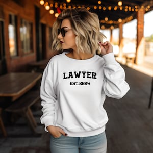 May include: White sweatshirt with black text that reads "LAWYER EST. 2024".