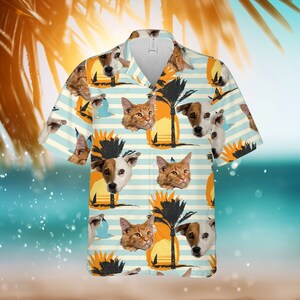Op de afbeelding: Een wit en blauw gepatroneerd overhemd met knopen met een herhalend patroon van een palmboom, een zonsondergang en de gezichten van een kat en een hond.