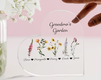 May include: A clear acrylic heart-shaped plaque with the text "Grandma's Garden" at the top.  Five different types of flowers are displayed with the names "Elena", "Margareth", "Miray", "Frank", and "Janin" written below each flower.