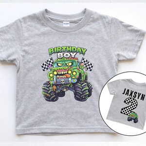 May include: A gray short-sleeved t-shirt featuring a green monster truck with the text "BIRTHDAY BOY". A smaller image shows a gray shirt with the name "JAXSYN" and the number "2".