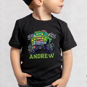 May include: Black t-shirt with a green monster truck and zombie design. The truck has large tyres and the name "ANDREW" in green. Checkered flags are on the side of the truck.