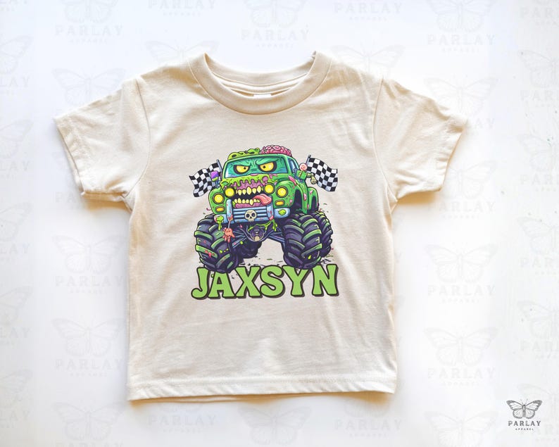 Puede incluir: Camiseta de manga corta color crema con un gr&aacute;fico de cami&oacute;n monstruo verde con tem&aacute;tica zombi. El cami&oacute;n tiene neum&aacute;ticos grandes, un cerebro y una lengua. El nombre "JAXSYN" est&aacute; impreso en verde debajo.
