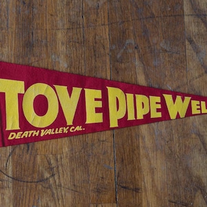 May include: Vintage pennant with red felt background and yellow lettering. The pennant reads "Stove Pipe Wells Death Valley, Cal."