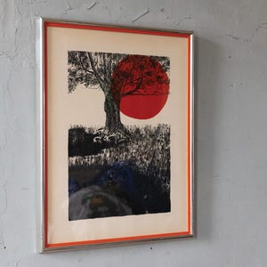 May include: Framed artwork featuring a tree silhouette with a large red sun. The artwork has a black and white tree with a red sun in the background. The frame is silver with an orange border. The artwork is mounted on a light beige background.