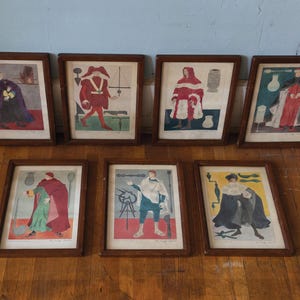 May include: A set of seven framed prints featuring historical figures in colorful garments, each accompanied by various tools and objects. The prints are enclosed in matching dark brown wooden frames and arranged in two rows.