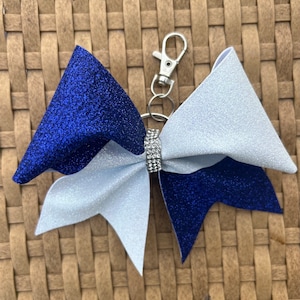 Peut inclure: Un nœud de pom-pom de cheer bleu et blanc avec un centre en strass argenté attaché à un porte-clés argenté.