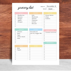 May include: A printed grocery list with sections for fruits, vegetables, protein, frozen items, baked goods, dairy, and household items. The list includes a budget of $300 and the week of November 6. The title "grocery list" is written in cursive.