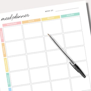 May include: A white meal planner with the words "meal planner" in a handwritten font. The planner has boxes for each day of the week, with sections for breakfast, lunch, dinner, and snacks. A black and silver pen rests on the planner.
