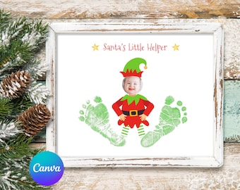 May include: A white frame with a white mount surrounding a white background with a green and red elf costume with a child's face in the head hole. The elf is standing with green footprints on either side. The text "Santa's Little Helper" is at the top of the image.