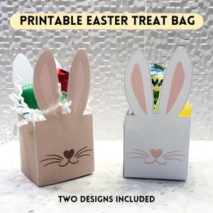 May include: Printable Easter treat bag template with two designs. One design features a white bunny with pink ears and the other features a brown bunny with pink ears. Both designs include a heart-shaped nose and whiskers.