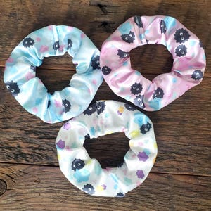 May include: Three colorful hair scrunchies with a black and white print of a cartoon character. The scrunchies are made of a soft, stretchy fabric and are perfect for holding hair in place.
