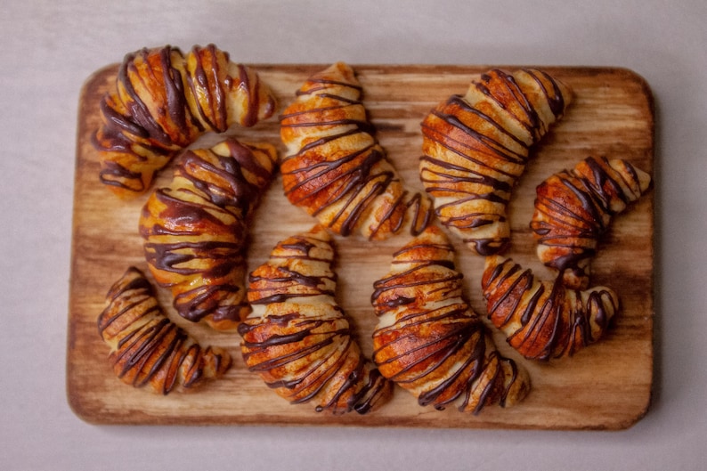 May include: A wooden cutting board with nine chocolate-covered croissants. The croissants are arranged in a semi-circle shape, with the tips of the croissants pointing towards the center of the board.