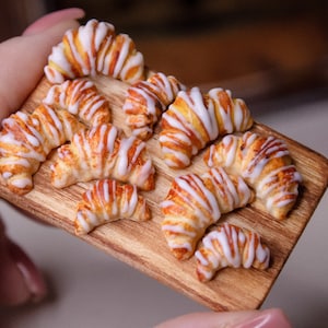 May include: A wooden board with nine miniature croissants, each with a white icing swirl. The croissants are arranged in a semi-circle on the board.