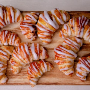 May include: A wooden board with nine crescent-shaped pastries topped with white icing. The pastries are arranged in a random pattern on the board.