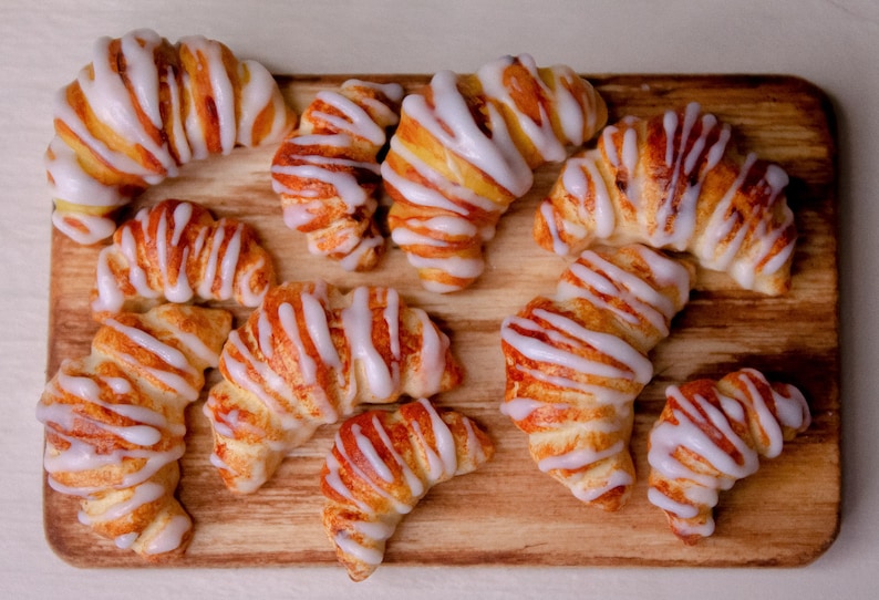 May include: A wooden board with nine crescent-shaped pastries topped with white icing. The pastries are arranged in a random pattern on the board.