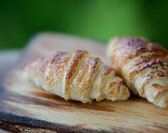 May include: Two golden brown croissants on a wooden cutting board. The croissants are slightly overlapping and have a flaky texture.