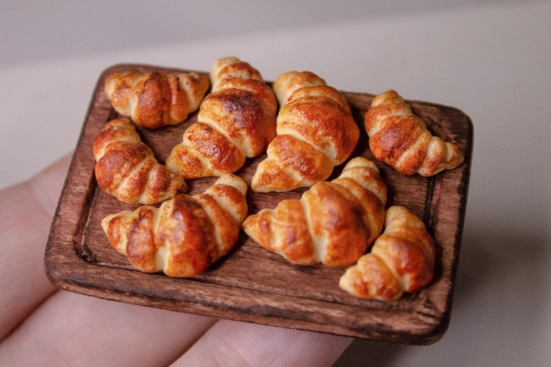 May include: A wooden serving board with eight miniature croissants. The croissants are golden brown and have a flaky texture.