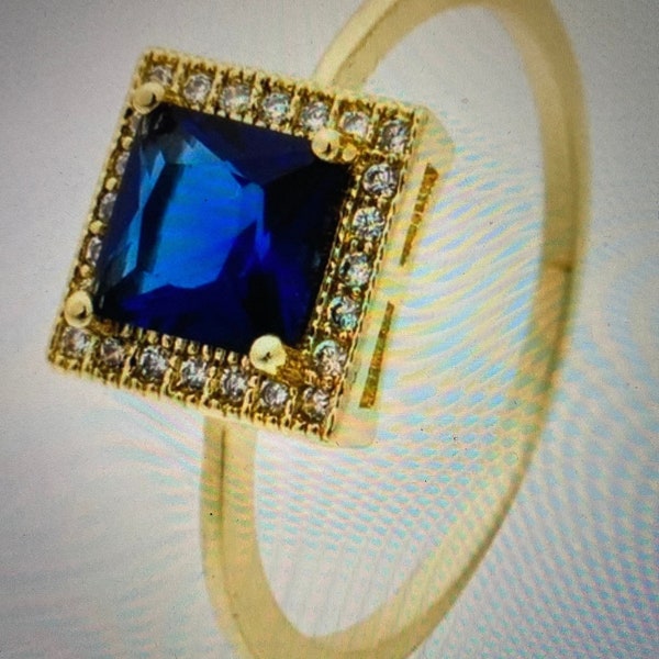 This ring is exquisitely beautiful with its gold-plated band and square halo adorned with  Lab-Created blue sapphire and clear gems.