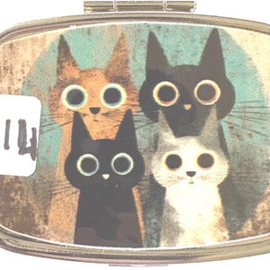 May include: A small, rectangular pill box with a hinged lid. The box features a whimsical illustration of four cats with large, round eyes in shades of orange, black, and gray against a teal background. A white sticker with the number 14 is on the left.