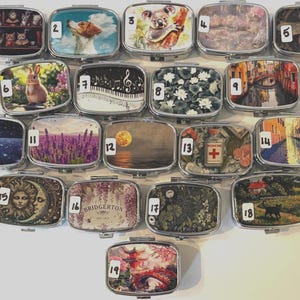 Puede incluir: Una colecci&oacute;n de diecinueve pastilleros rectangulares de metal, cada uno con una imagen decorativa diferente en la tapa. Las im&aacute;genes incluyen animales, paisajes y dise&ntilde;os art&iacute;sticos. Los pastilleros est&aacute;n dispuestos en una cuadr&iacute;cula.