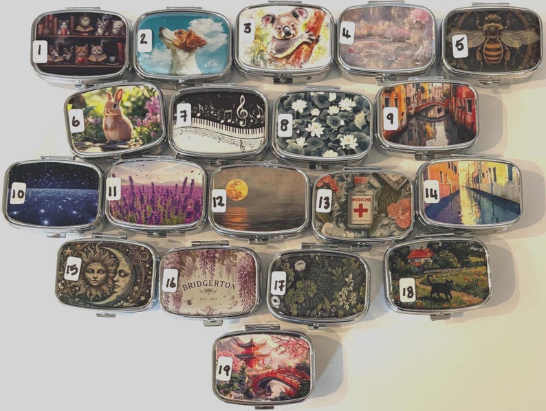 Puede incluir: Una colecci&oacute;n de diecinueve pastilleros rectangulares de metal, cada uno con una imagen decorativa diferente en la tapa. Las im&aacute;genes incluyen animales, paisajes y dise&ntilde;os art&iacute;sticos. Los pastilleros est&aacute;n dispuestos en una cuadr&iacute;cula.