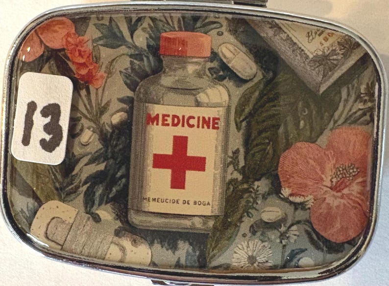 Puede incluir: Peque&ntilde;a caja rectangular con bordes plateados, con tem&aacute;tica m&eacute;dica vintage. El interior presenta una botella con la etiqueta "MEDICINE" con una cruz roja, pastillas y elementos florales. Tambi&eacute;n es visible el n&uacute;mero "13".