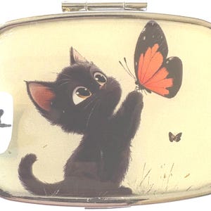 May include: A rectangular, hinged pill box with a cartoon illustration of a black kitten reaching for a butterfly with orange and black wings. The background is a light yellow color. The number 7 is on a white sticker in the corner.