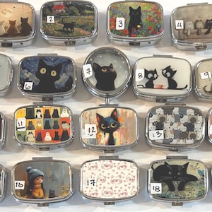 May include: A collection of rectangular, silver-toned pill boxes, each featuring a unique cat-themed design. The boxes showcase various cat illustrations, including black cats, kittens under an umbrella, and cat patterns. The designs are colorful and artistic.