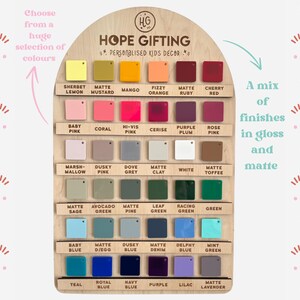 Op de afbeelding: Houten displaybord met een verscheidenheid aan kleurstalen in glanzende en matte afwerkingen. Het bord toont de tekst "HOPE GIFTING - PERSONALISED KIDS DECOR" en een selectie kleuren, waaronder Sherbet Lemon, Baby Pink en Teal.