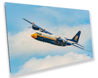 May include: A photograph of a blue and yellow C-130 Hercules aircraft, with the words "Blue Angels" and "United States Navy" visible. The aircraft is in flight against a backdrop of a cloudy blue sky.