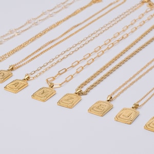 May include: A set of gold necklaces with medallions featuring different letters of the alphabet. The necklaces are arranged in a row, with the medallions facing the viewer. The text "MEDAL INITIAL NECKLACE" is printed below the necklaces.