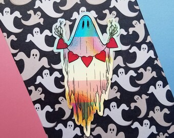 May include: A rainbow-coloured ghost with a heart garland and skeletal hands. The ghost is on a black background with a pattern of white ghosts.