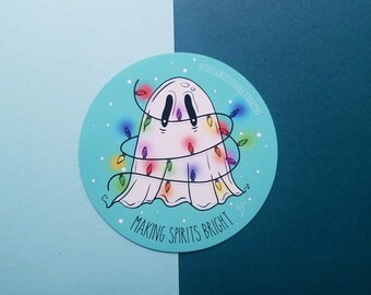 May include: A white ghost with a rainbow string of lights wrapped around it. The ghost is on a blue background with white snowflakes. The text "Making Spirits Bright" is below the ghost. The text "@toilandtroublecreative" is at the top of the image.