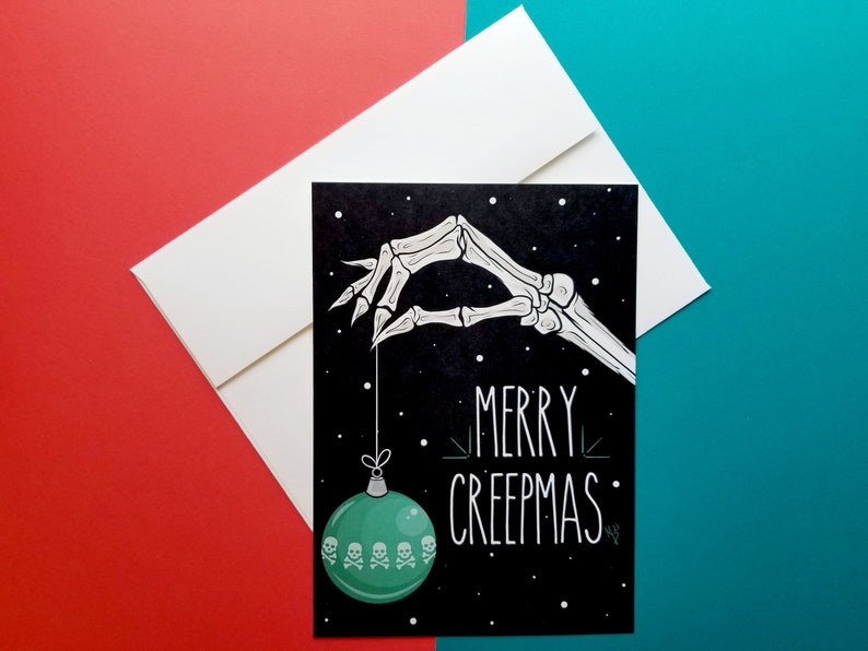 May include: A black and white illustration of a skeleton hand holding a green Christmas ornament with skulls on it. The text "Merry Creepmas" is written in white on a black background.
