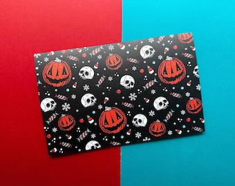 May include: A black card with a Halloween-themed pattern featuring orange jack-o'-lanterns, white skulls, candy, and snowflakes. The card is set against a red and blue background.