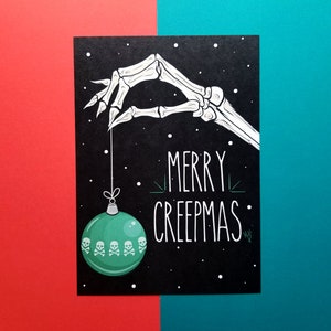 May include: A black card with a white skeleton hand holding a green Christmas ornament with skull and crossbones. The card says "Merry Creepmas".