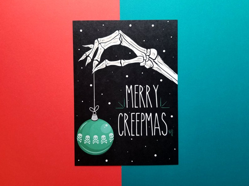 May include: A black card with a white skeleton hand holding a green Christmas ornament with skull and crossbones. The card says "Merry Creepmas".
