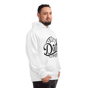 Może przedstawiać: Biała bluza z kapturem z przednią kieszenią i kapturem ze sznurkiem. Bluza z kapturem ma czarną grafikę z napisem "Best Dad Ever" w okrągłym wzorze. Osoba ma na sobie białą bluzę z kapturem.