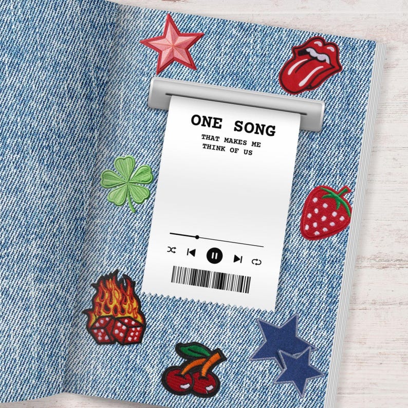 May include: A denim-textured notebook with various embroidered patches. Patches include a red star, a four-leaf clover, a strawberry, a pair of cherries, a flaming dice, a blue star, and a red tongue. A receipt-like paper reads "ONE SONG THAT MAKES ME THINK OF US".