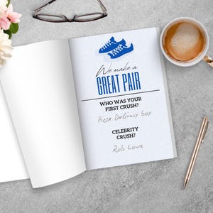 Puede incluir: Un libro abierto con el texto "We make a GREAT PAIR" y preguntas sobre flechazos. Un gr&aacute;fico de zapatillas azules est&aacute; en la parte superior. Una taza de caf&eacute;, un bol&iacute;grafo y gafas tambi&eacute;n est&aacute;n en la superficie gris.