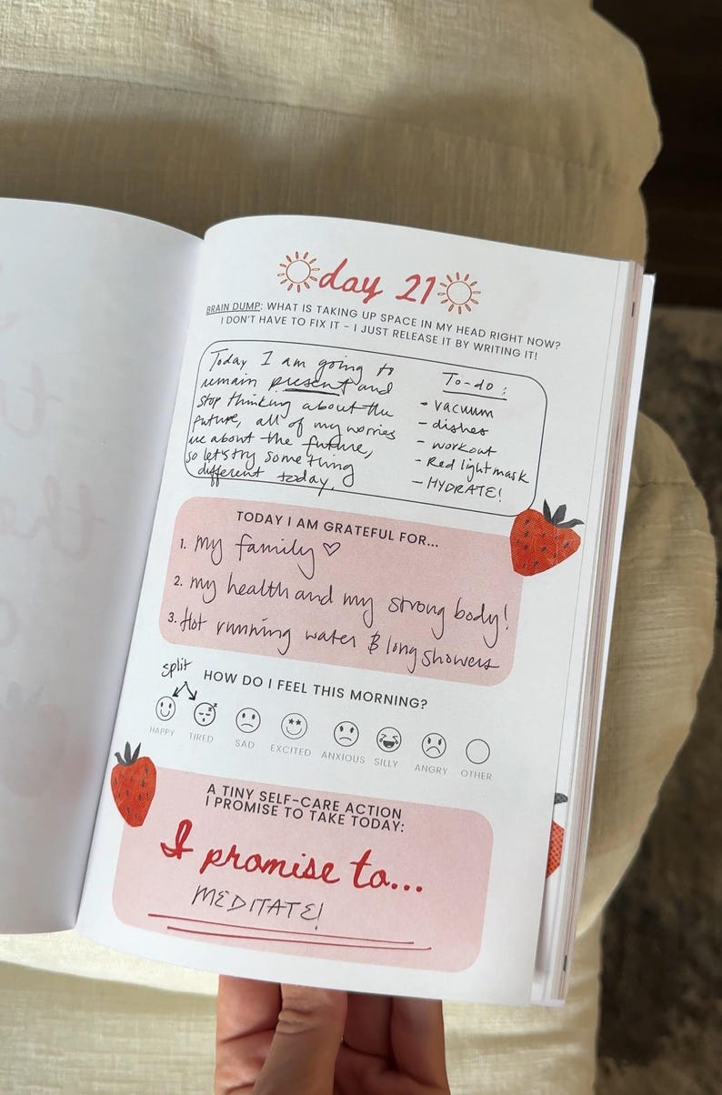 K&ouml;nnte beinhalten: Ge&ouml;ffnete Tagebuchseite mit handschriftlichen Notizen und Aufforderungen zur Selbstreflexion. Die Seite enth&auml;lt die &Uuml;berschrift "Tag 21" und Abschnitte f&uuml;r ein Brain Dump, eine To-Do-Liste und Dankbarkeit. Dekorative Erdbeer-Illustrationen sind vorhanden.